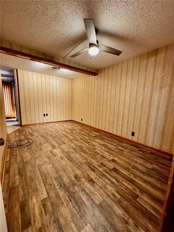 unfurnished room featuring a textured ceiling, wood walls, ceiling fan, and wood-type flooring