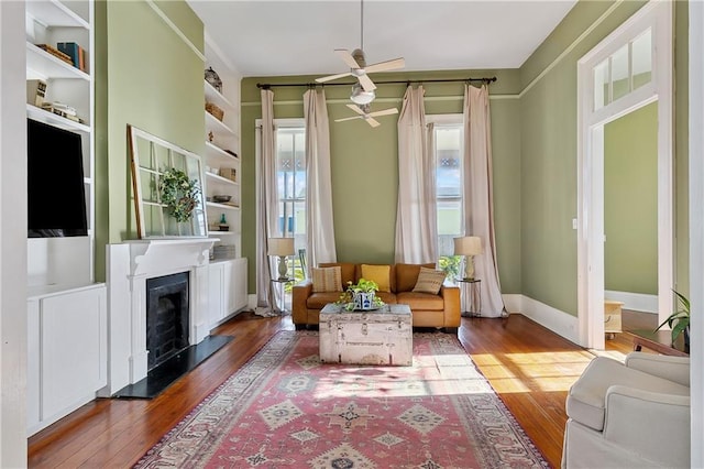 living area with built in shelves, ceiling fan, and hardwood / wood-style flooring