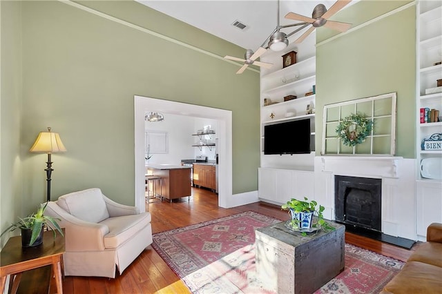 living room with wood-type flooring, ceiling fan, and built in shelves