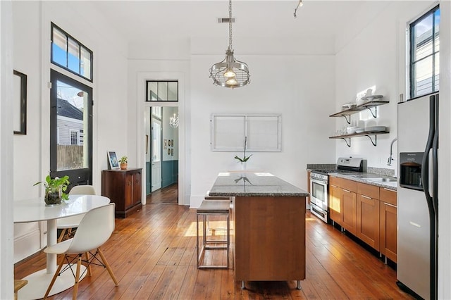 kitchen featuring stainless steel appliances, decorative light fixtures, a center island, stone counters, and hardwood / wood-style flooring