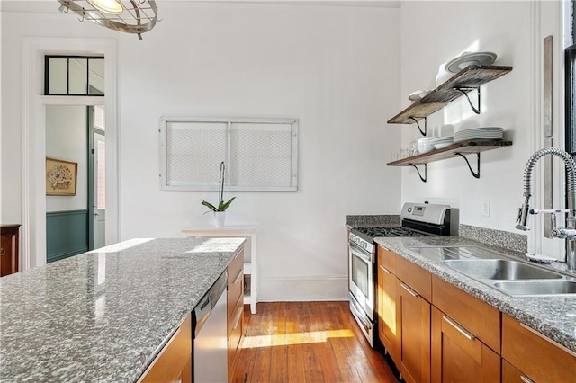 kitchen featuring stainless steel appliances, light hardwood / wood-style floors, dark stone countertops, and sink