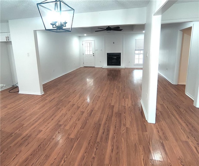 unfurnished living room with ceiling fan with notable chandelier, a fireplace, a textured ceiling, and dark wood-type flooring