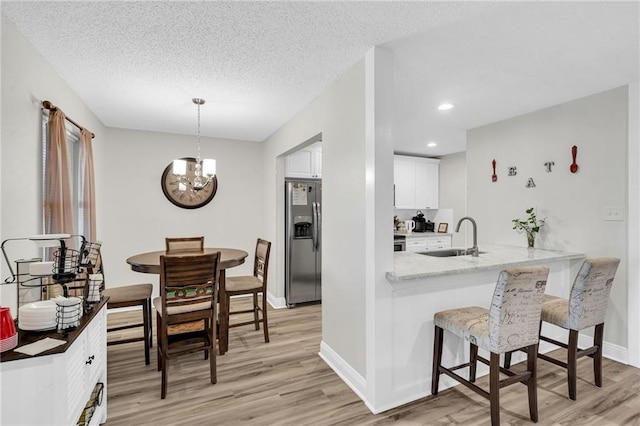 kitchen featuring sink, white cabinets, decorative light fixtures, kitchen peninsula, and stainless steel fridge with ice dispenser