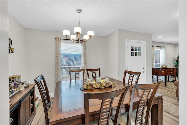 dining area with an inviting chandelier, light wood-type flooring, and a textured ceiling