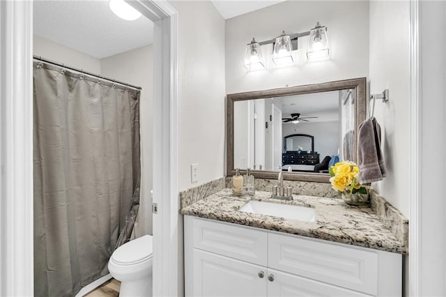 bathroom with toilet, a textured ceiling, walk in shower, ceiling fan, and vanity