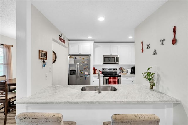 kitchen with a breakfast bar area, stainless steel appliances, light stone countertops, sink, and white cabinetry