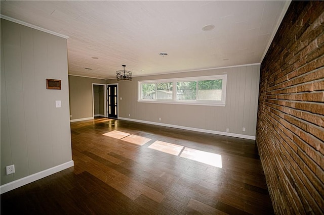 spare room featuring wooden walls, ornamental molding, brick wall, dark hardwood / wood-style flooring, and a chandelier