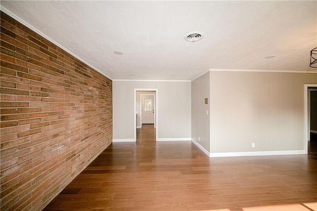 empty room featuring crown molding, brick wall, and wood-type flooring