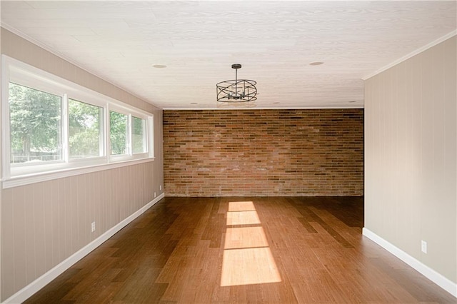 empty room with brick wall, ornamental molding, wood-type flooring, and wooden walls