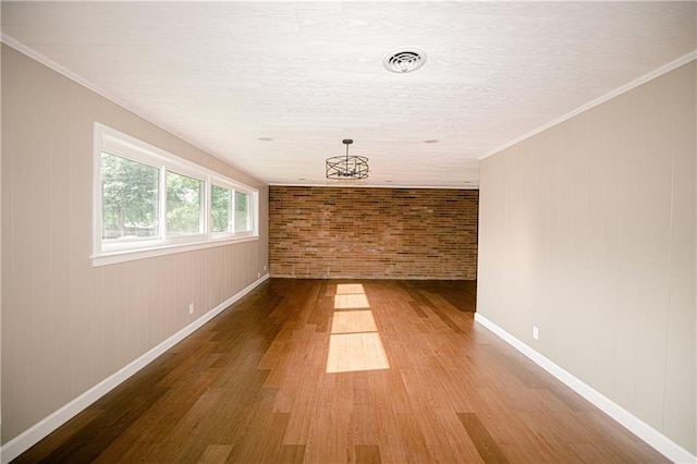 spare room with ornamental molding, a chandelier, brick wall, and wood-type flooring