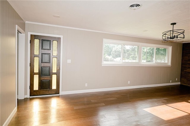 empty room with a notable chandelier, ornamental molding, wooden walls, and hardwood / wood-style floors