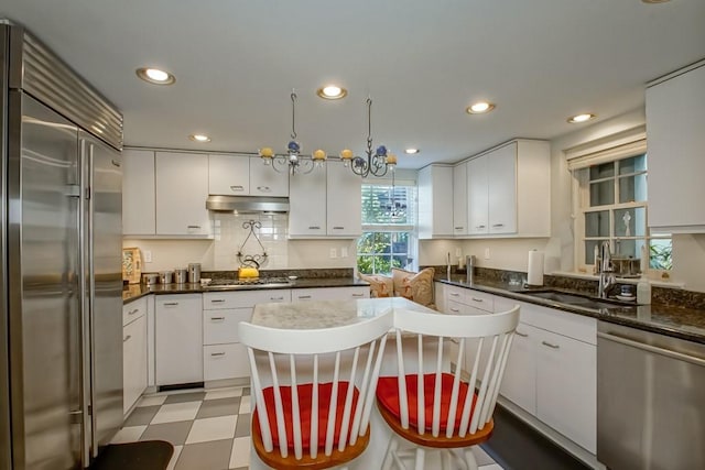 kitchen with stainless steel appliances, white cabinetry, sink, and hanging light fixtures