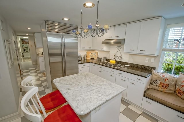 kitchen with stainless steel appliances, a notable chandelier, a kitchen island, white cabinetry, and dark stone counters