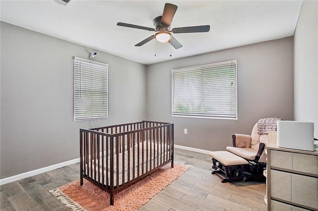 bedroom featuring ceiling fan, hardwood / wood-style floors, and a nursery area