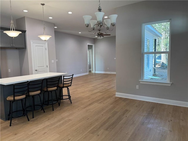 kitchen featuring gray cabinets, light wood-type flooring, a kitchen island, decorative light fixtures, and ceiling fan with notable chandelier