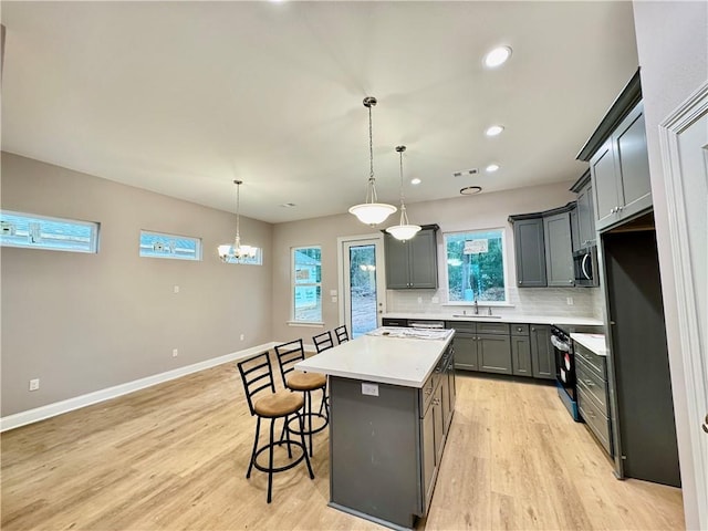 kitchen with tasteful backsplash, gray cabinets, a kitchen island, pendant lighting, and appliances with stainless steel finishes