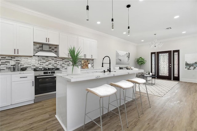 kitchen featuring a kitchen island with sink, white cabinets, stove, and wall chimney exhaust hood