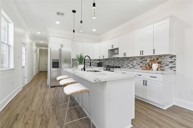 kitchen featuring a kitchen island with sink, stainless steel fridge, hanging light fixtures, and white cabinetry