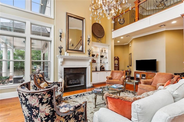 living room with a towering ceiling, a notable chandelier, a premium fireplace, and light wood-type flooring