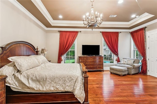 bedroom with a raised ceiling, a chandelier, hardwood / wood-style floors, and ornamental molding