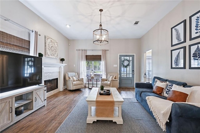 living room featuring dark hardwood / wood-style flooring, a tiled fireplace, and a notable chandelier