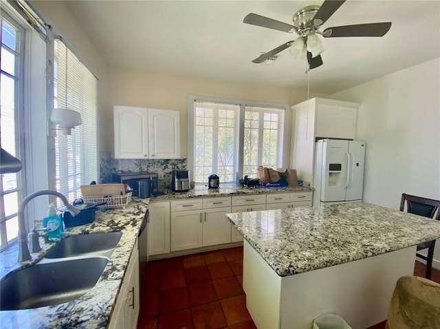 kitchen with tasteful backsplash, white refrigerator with ice dispenser, white cabinetry, and a sink