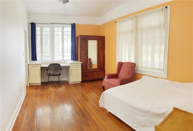 bedroom featuring baseboards, built in study area, and hardwood / wood-style floors