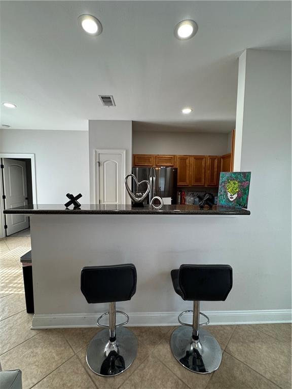 kitchen featuring a breakfast bar area, light tile patterned flooring, stainless steel fridge, and kitchen peninsula