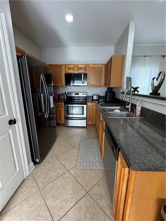 kitchen with sink, appliances with stainless steel finishes, dark stone countertops, and light tile patterned flooring