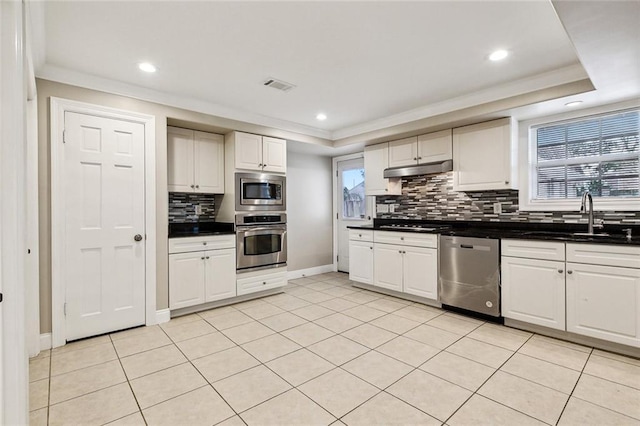 kitchen with sink, stainless steel appliances, light tile patterned floors, and a tray ceiling