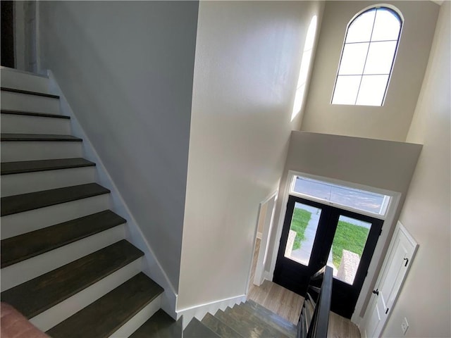 foyer entrance with stairway, french doors, a towering ceiling, and wood finished floors