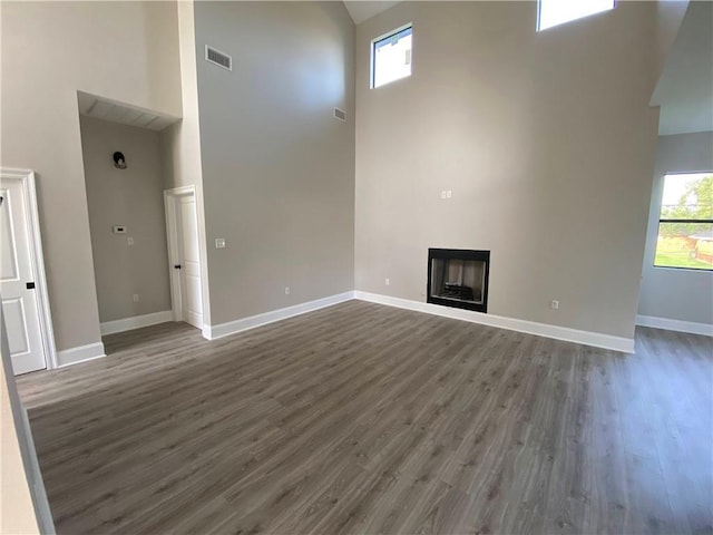 unfurnished living room featuring dark wood-style floors, visible vents, baseboards, a fireplace, and a towering ceiling