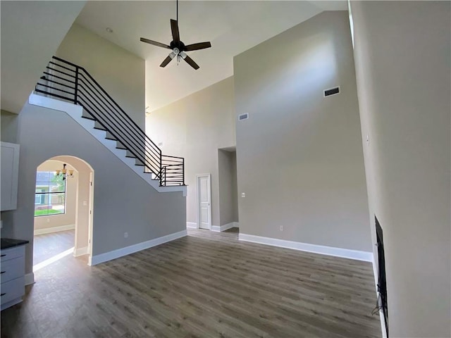 unfurnished living room with wood finished floors, arched walkways, baseboards, ceiling fan, and stairs