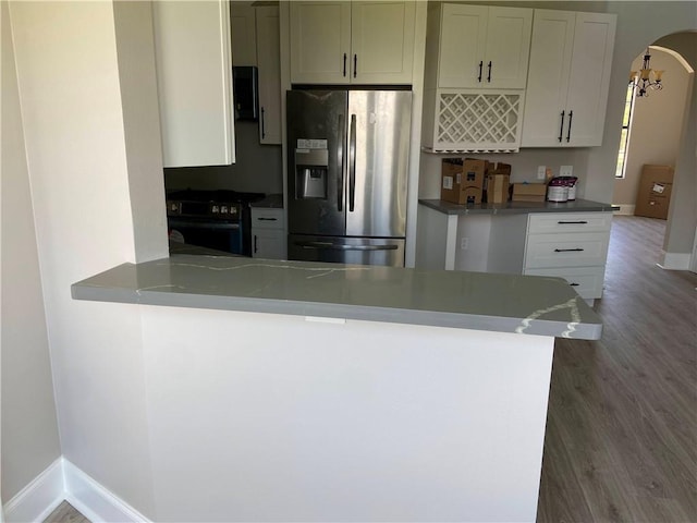 kitchen with wood finished floors, baseboards, arched walkways, black range with gas cooktop, and stainless steel fridge