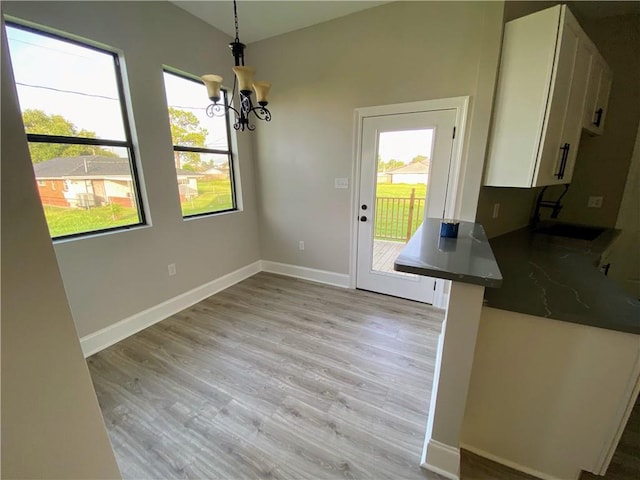 unfurnished dining area featuring an inviting chandelier, baseboards, and light wood-type flooring