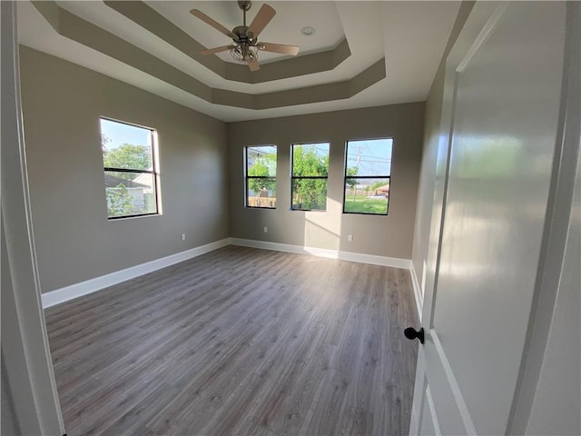 unfurnished room with a ceiling fan, a tray ceiling, wood finished floors, and baseboards