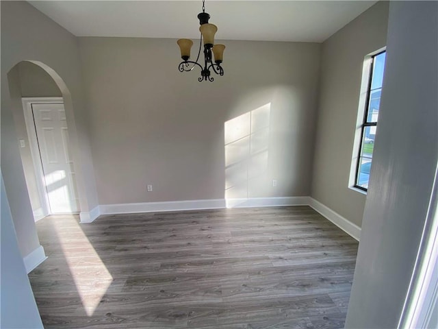 spare room featuring baseboards, arched walkways, wood finished floors, and a chandelier