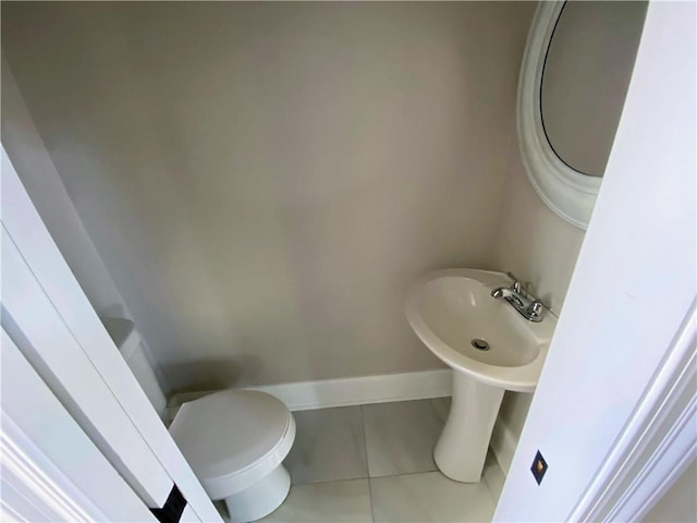 half bath featuring tile patterned floors, toilet, baseboards, and a sink