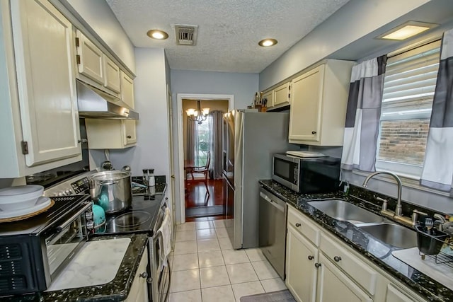 kitchen featuring sink, a textured ceiling, light tile patterned flooring, dark stone countertops, and appliances with stainless steel finishes