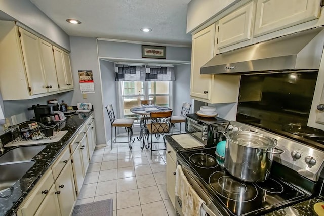 kitchen featuring stainless steel electric range oven, cream cabinets, and light tile patterned floors