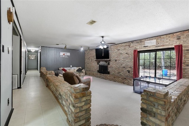 living room with a brick fireplace, brick wall, ceiling fan, and a textured ceiling