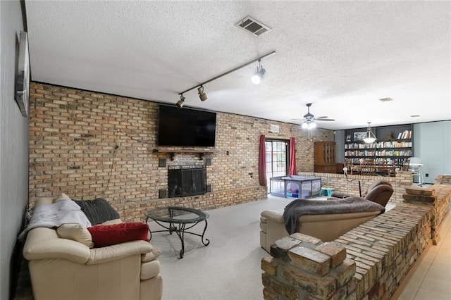 living room featuring a textured ceiling, a fireplace, ceiling fan, track lighting, and brick wall