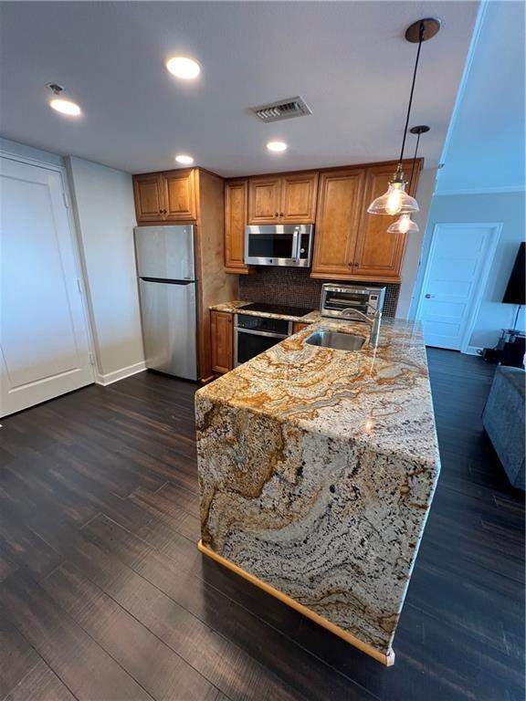 kitchen featuring dark hardwood / wood-style floors, pendant lighting, sink, appliances with stainless steel finishes, and light stone counters