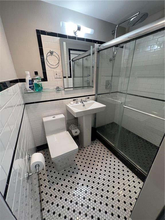 bathroom featuring an enclosed shower, tile patterned flooring, sink, tile walls, and toilet