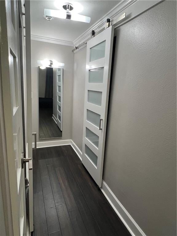 hallway featuring dark wood-type flooring, crown molding, and a barn door