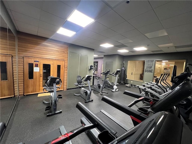 gym featuring a drop ceiling and wood walls