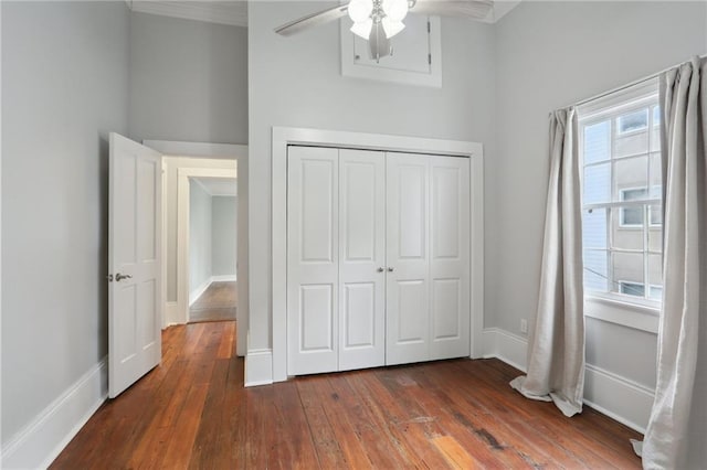 unfurnished bedroom with ceiling fan, crown molding, dark hardwood / wood-style flooring, and a closet