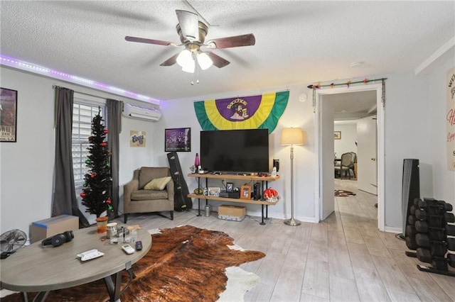 living room featuring ceiling fan, a wall unit AC, a textured ceiling, and light wood-type flooring