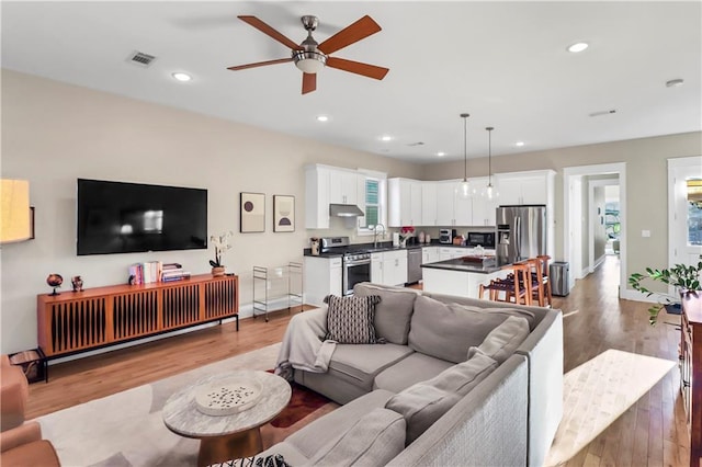 living room with ceiling fan, sink, and light hardwood / wood-style flooring