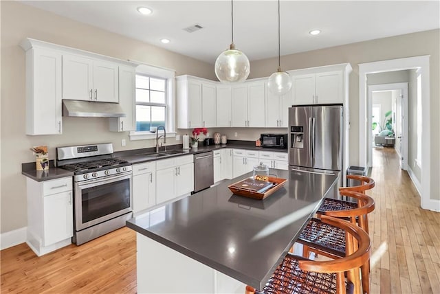 kitchen with pendant lighting, sink, white cabinets, a kitchen bar, and stainless steel appliances